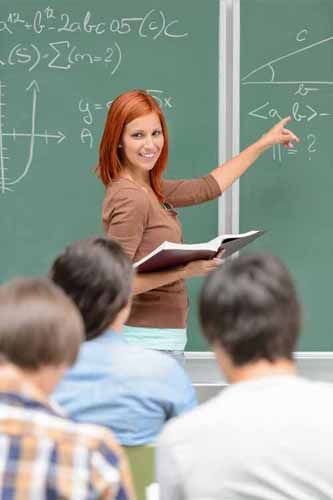 A Postsecondary teacher points to a chalkboard in front of a class